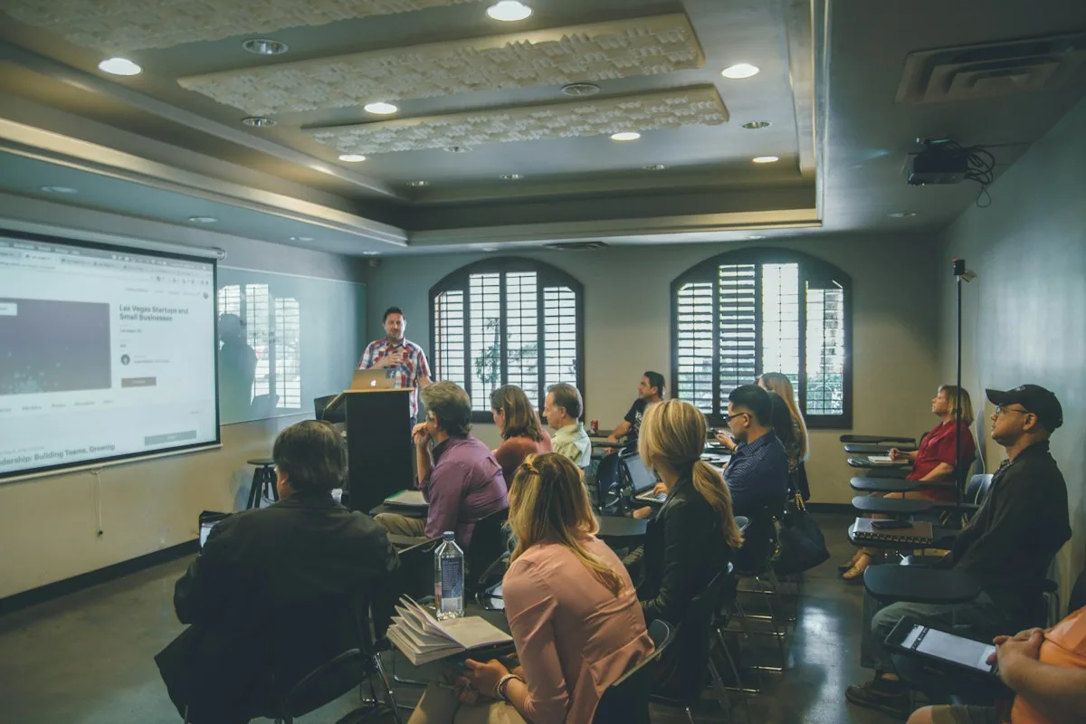 Adult learners in a training room facing a presenter and screen